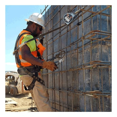 A construction worker wearing a hard hat and high-visibility vest uses tools to fix rebar on a concrete structure, ensuring it remains corrosion resistant. The worker is secured with a French Creek Renegade SRL RG3-13-0Z self-retracting lifeline and safety harness, safely stationed outdoors on a bustling construction site.