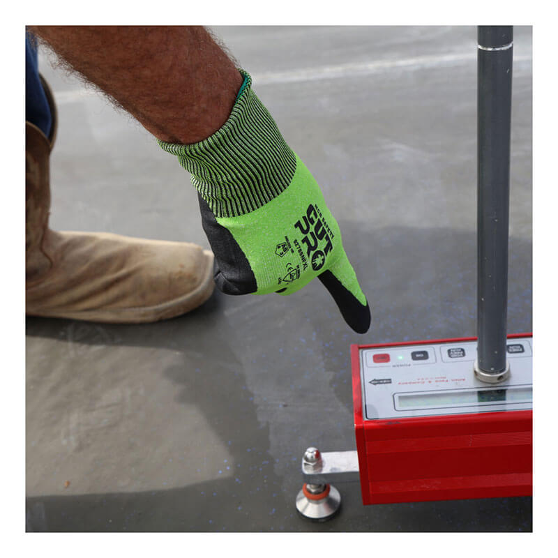 A person wearing MCR Safety CutPro HyperMax MicroFoam Nitrile Gloves 92785NF presses a button on a red electronic measuring device on concrete. Their boot and part of their leg are also visible.