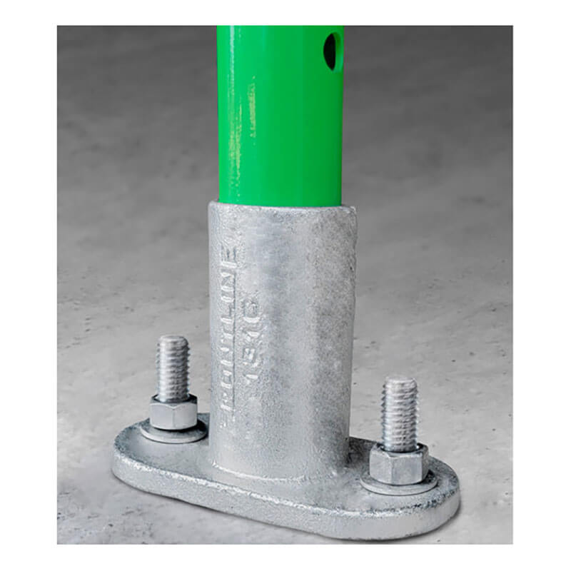 A green metal post from the Frontline Fixed Guardrail System for Concrete/Steel Substrates by Frontline Fall Protection is anchored to concrete with a silver galvanized base plate, stamped text, and secured using two large nuts and bolts.