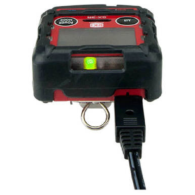 A close-up of the RKI Instruments GX-3R Bundle, a red and black gas monitor with a display, glowing green indicator light, and a black cable connected—ideal for confined space gas detection.