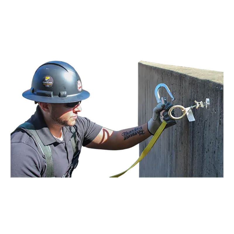 A construction worker in a hard hat, safety glasses, and harness attaches a French Creek Production Concrete Hole Anchor 1770 to a concrete surface for fall protection.