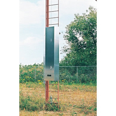 A tall metal electrical cabinet is mounted outdoors on a red tower, with a 3M DBI-SALA Lad-Saf Ladder Gate 5901980 by 3M Fall Protection nearby, against a backdrop of grass, trees, and a chain-link fence under a partly cloudy sky.