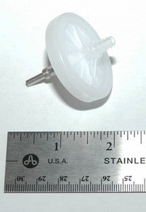 A RAE Systems External Filter 002-3022-005, which is circular and white, is positioned on a white surface. Beside it lies a metal ruler marked in both inches and centimeters, indicating the filter's diameter to be approximately 2 inches—ideal for precise gas detection applications.