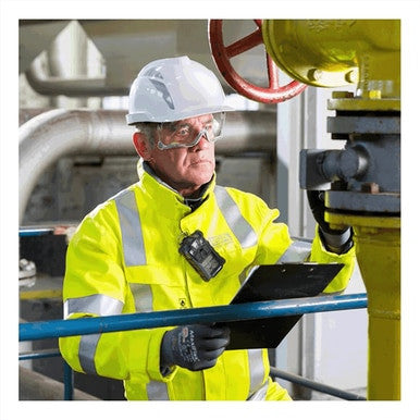 A worker in high-visibility gear inspects equipment at a plant using the MSA Safety ALTAIR 4XR Multigas Detector 10178557 with XCell sensors and Bluetooth, while holding a clipboard.