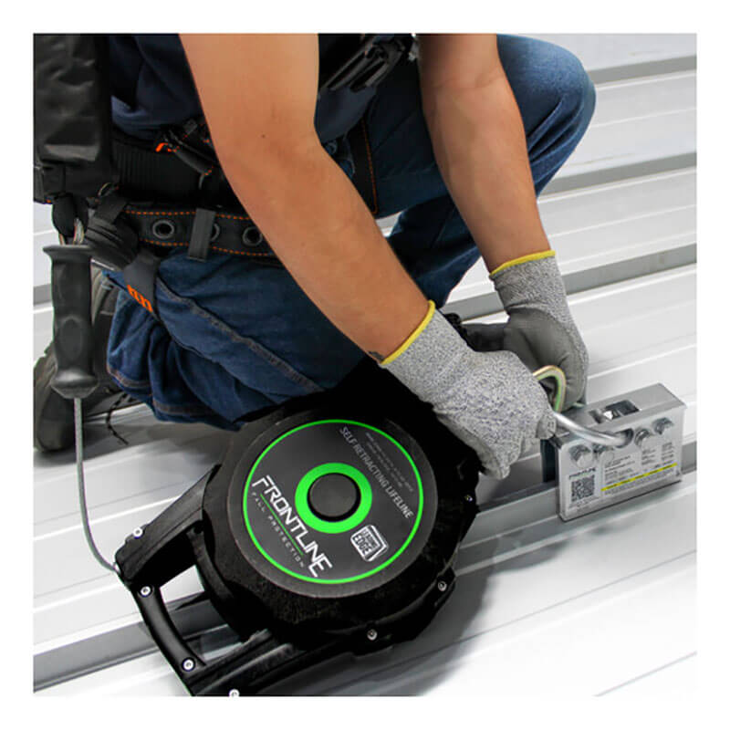 Wearing safety gloves and a harness, a user installs the Frontline Fall Protection 2-Way Standing Seam Roof Anchor RO2W on a metal roof, securing a self-retracting lifeline to its non-penetrating anchor for fall protection.