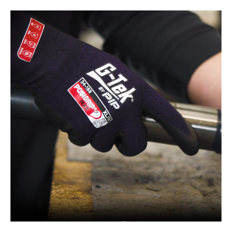A person wearing PIP G-Tek PosiGrip MAX Nylon/Spandex Gloves (model 34-188) is gripping a cylindrical metal object over a wooden work surface.