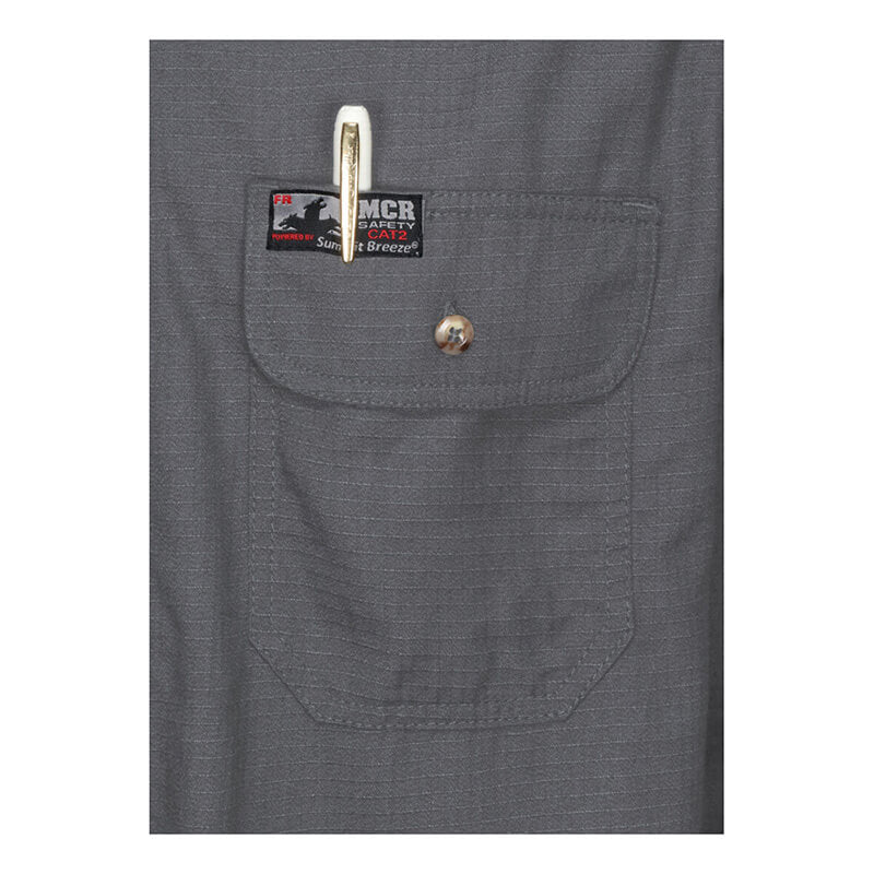 Close-up of a gray MCR Summit Breeze 5.5 oz FR Shirt SBS100_ pocket with flap, button, and pen. A black and red "MCR Safety" label above the pocket highlights arc flash protection for enhanced safety.