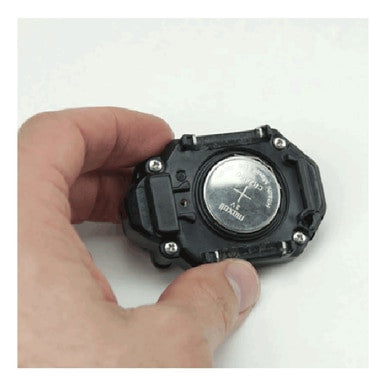 A hand holds a digital watch's back cover, showing the battery compartment. Inside, a silver circular cell battery with a plus sign sits securely with four tiny screws. The design mirrors the precision and functionality of RKI Instruments' Replacement CO Sensor ESR-A13P-CO.