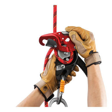 A person wearing brown leather gloves operates a Petzl I'D L Self-Braking Descender (Large, by Petzl), colored red and black, which is attached to a red climbing rope with black markings.