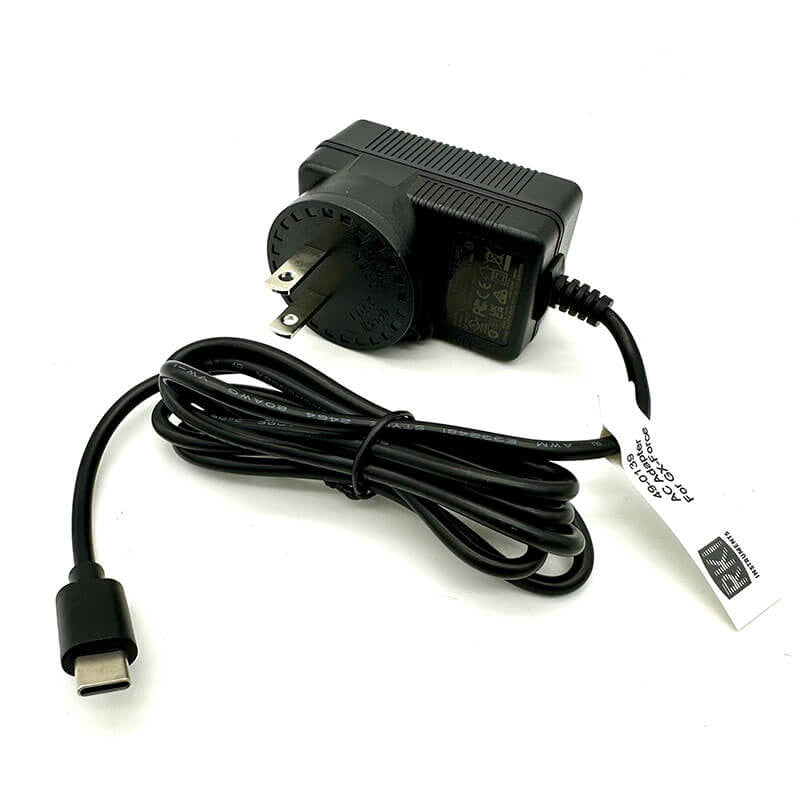 The RKI Instruments GX-Force 100-240 VAC AC Adapter (49-0139) features a standard two-prong plug, long attached cord, and USB-C connection. A label with technical specifications is included.