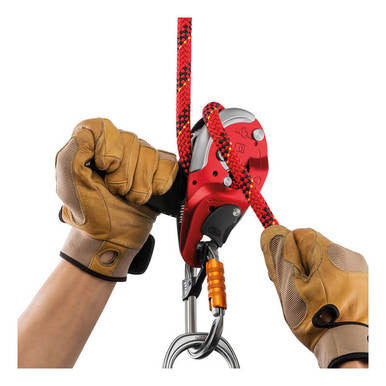 Wearing tan protective gloves, a person operates the Petzl I'D L Self-Braking Descender (Large Size) by Petzl, which is red and black with an anti-panic system, attached to a climbing rope and carabiner.