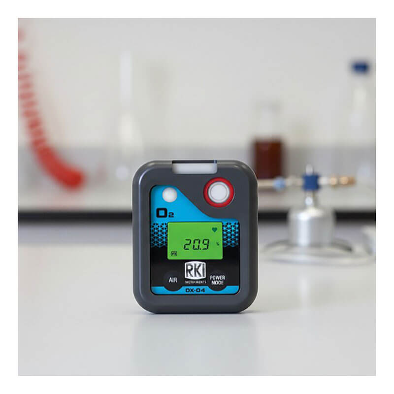 An RKI Instruments OX-04 Series O2 Single Gas Monitor 72-0018 with a digital display reading 20.9 rests on a laboratory table, with blurred lab equipment visible in the background.