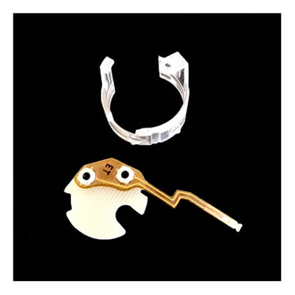A small, intricate electronic component featuring a gold circuit pathway and white elements is displayed against a black background. Above it, there is a clear plastic clip-like holder, resembling those used for the PK Safety Supply BW Micro Clip XT/XL Replacement Flex PCB MC2-FPCB1.