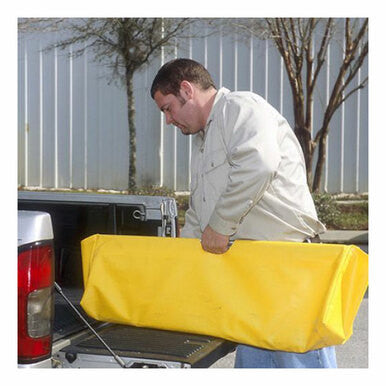 An individual is unloading an UltraTech Grate Lifter Carrying Case 9241, a large yellow rectangular bag, from the back of an UltraTech International pickup truck. The outdoor setting features a building with metal siding in the foreground and trees visible in the background.