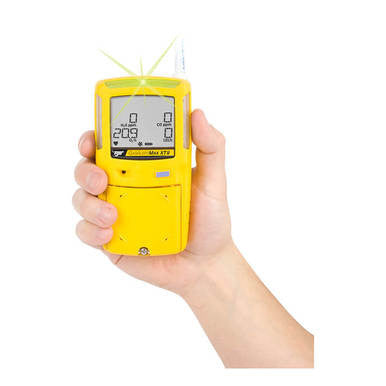 A hand holds the BW XT-XWHM-Y-NA Honeywell GasAlert Max XT II Confined Space Multi-Gas Monitor by PK Safety Supply, a yellow multi-gas monitor designed for hazardous spaces. Its gray display area shows numerical and graphical readings, with a green status light glowing at the top.
