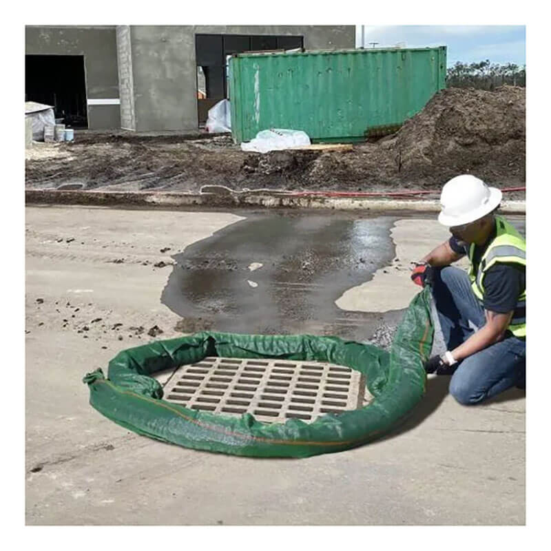 A construction worker in a safety vest and helmet installs an UltraTech Filter Sock 945_ around a storm drain on concrete, with water nearby and construction materials visible, for effective pollutant removal.