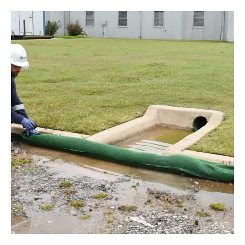 A worker in safety gear installs an UltraTech Filter Socks 945_ by UltraTech at the edge of a storm drain on grass, providing effective storm drain protection and helping to prevent water pollution.