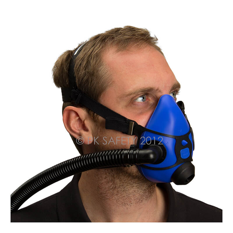 A person is wearing the Allegro Half Mask Constant Flow Airline Respirator 9920 from PK Safety Supply. The silicone blue facepiece, secured by elastic straps around their head, covers their nose and mouth with an attached black hose. They are looking to the side, ensuring continuous airflow.