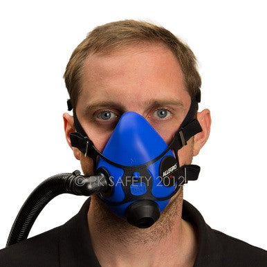 The man is confidently facing forward, dressed in a black shirt, while wearing the Allegro Half Mask Constant Flow Airline Respirator 9920 by PK Safety Supply. This blue mask features black straps and a side hose attachment for continuous airflow. The silicone facepiece covers his nose and mouth to ensure full protection.