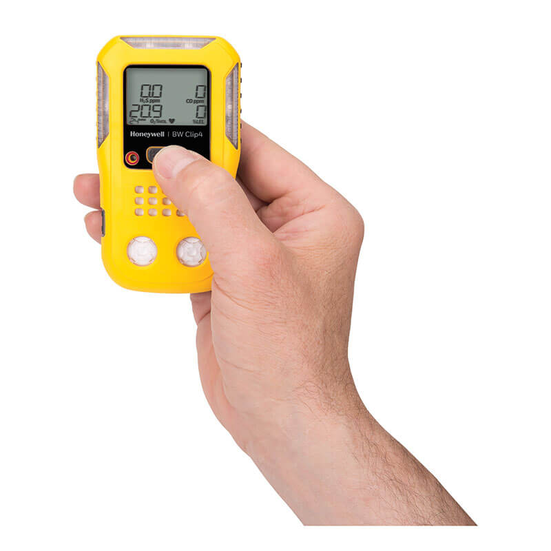 A hand holds the BW Technologies by Honeywell BW Clip4 4-Gas Detector BWC4-Y-N, with a thumb pressing a button and its digital display visible on this reliable yellow portable gas monitor.