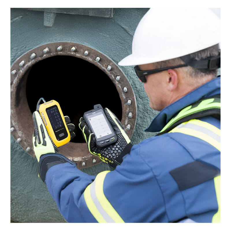 A worker in safety gear uses a BW Technologies by Honeywell BW UItra Gas Detector and another device to inspect the opening of industrial equipment or a tank.