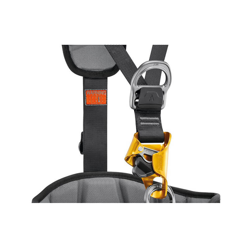 Close-up of the Petzl ASTRO International Harness C083BB0_ with black straps, a gray buckle, yellow attachment, and a visible warning label on the left strap. Ideal for rope access technicians and features 3D foam padding for comfort on long climbs.