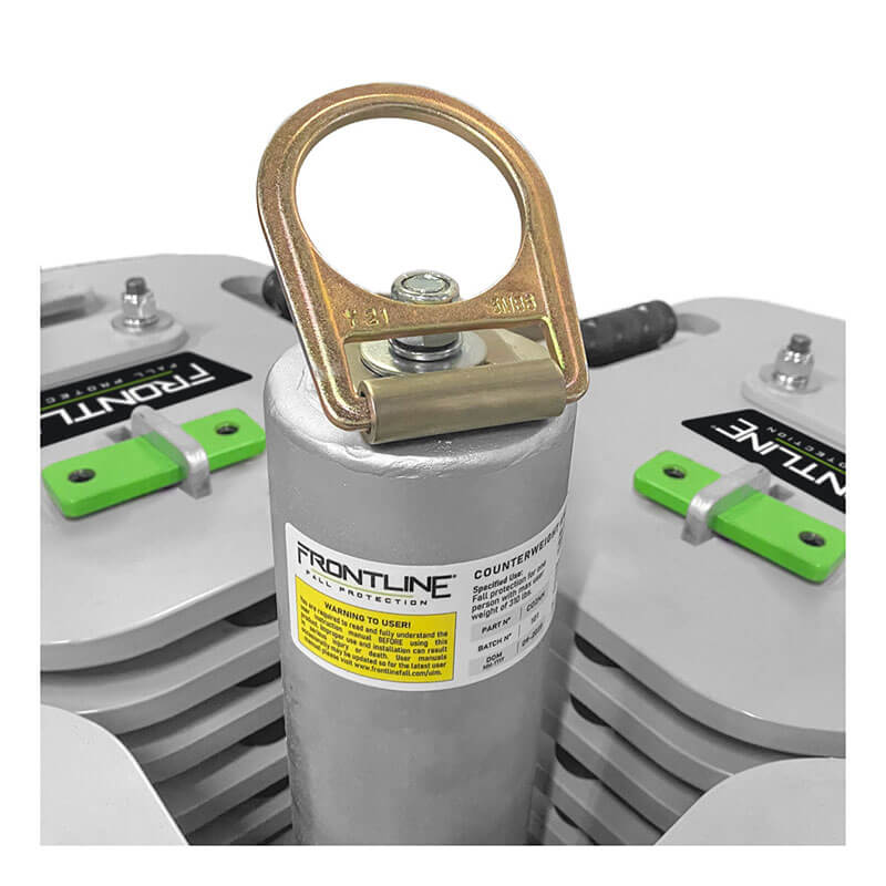 Close-up of the Frontline Commando Counterweight Fall Protection System CO2NN by Frontline Fall Protection, showing a metallic anchor point with a gold ring marked "FRONTLINE," attached to stacked weights with green handles and safety labels.