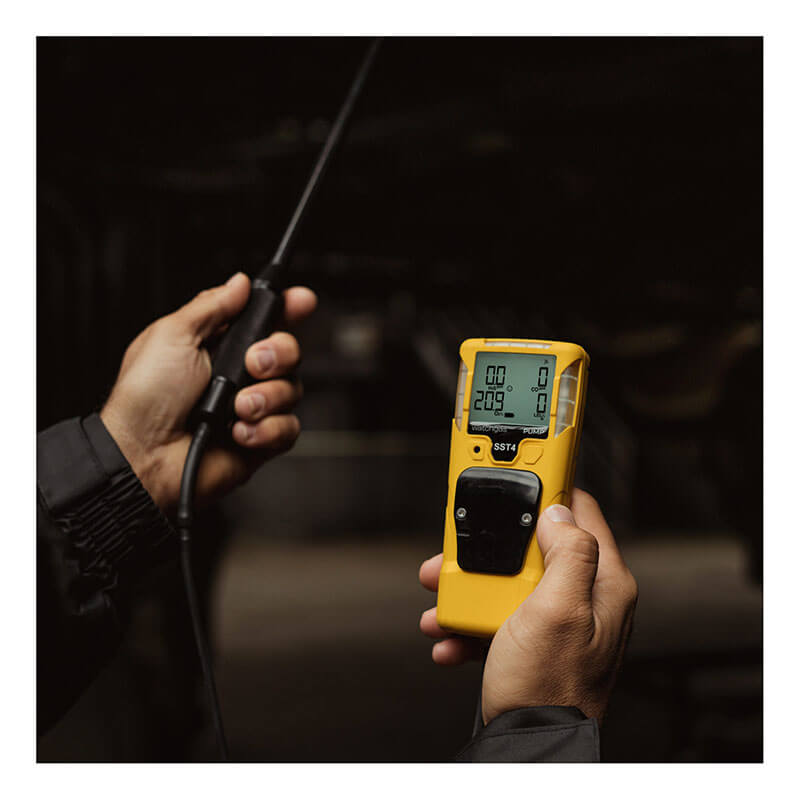A person holds a yellow WatchGas SST4-PUMP 4-Gas Detector by WatchGas, using its probe to detect gases and view digital readings in a dimly lit area.