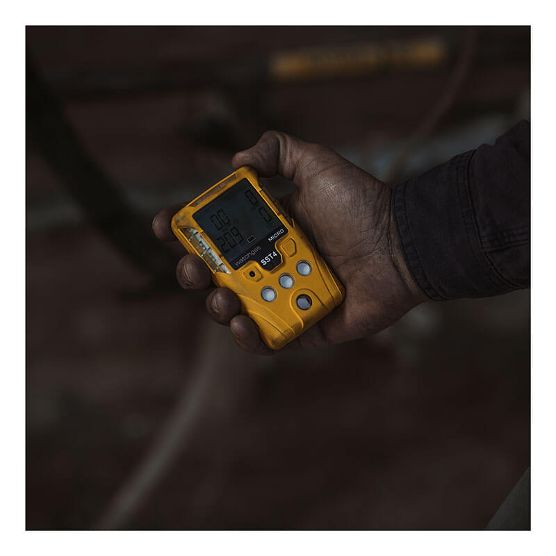 A person holds a yellow WatchGas SST1 Serviceable CH4S Gas Detector SST1-MM with a digital display, showing readings against a dark, blurred background.