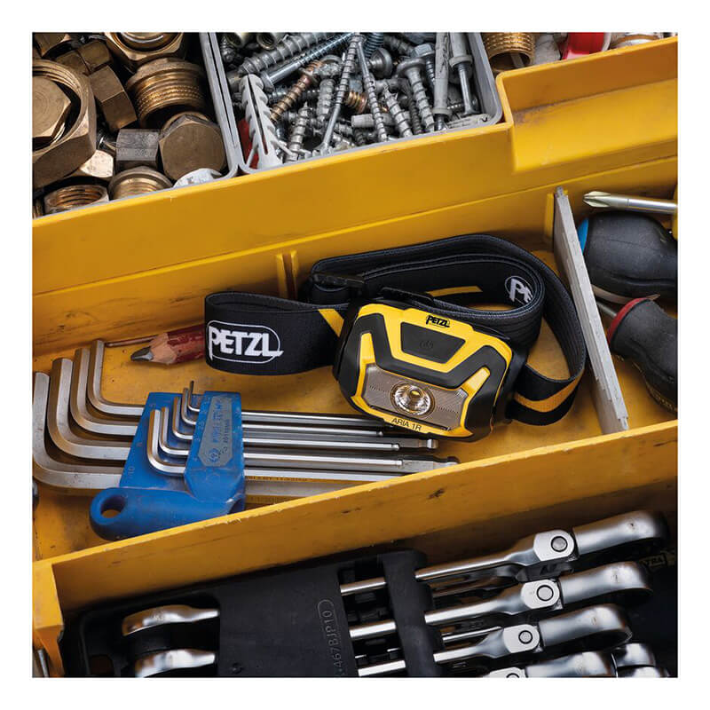 A yellow toolbox stocked with tools like hex keys, ratchets, screws, nuts, and a Petzl ARIA 1R Rechargeable Headlamp (E069CB00) featuring an adjustable strap for reliable job site lighting.