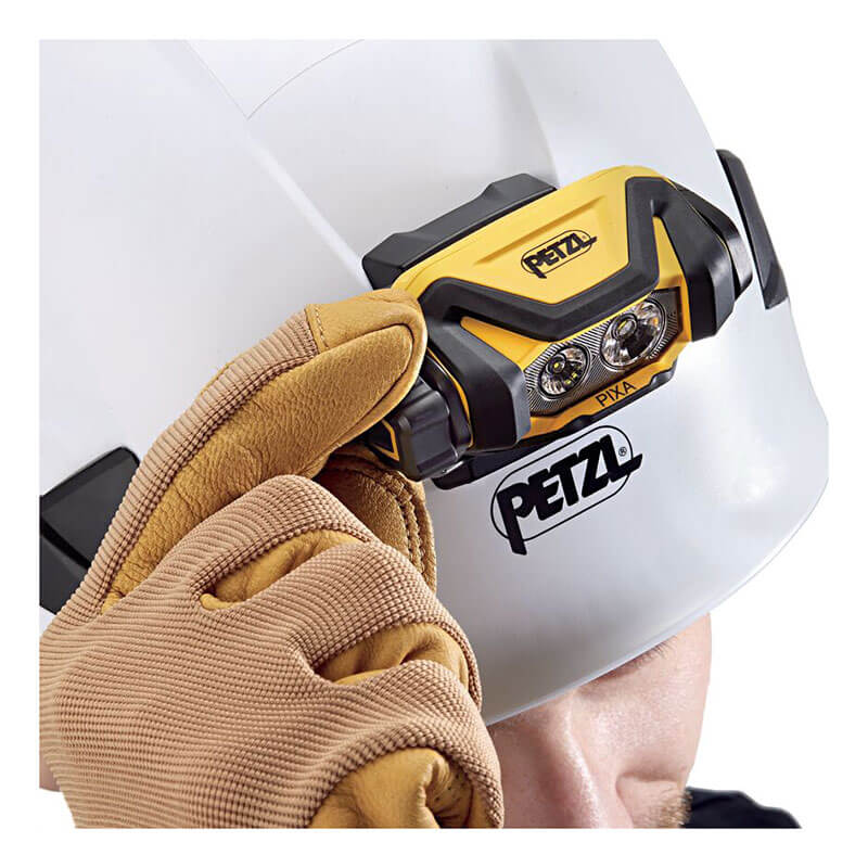 A person in a white Petzl safety helmet adjusts a yellow Petzl PIXA 4 Waterproof Headlamp E120AA00 while wearing brown work gloves.