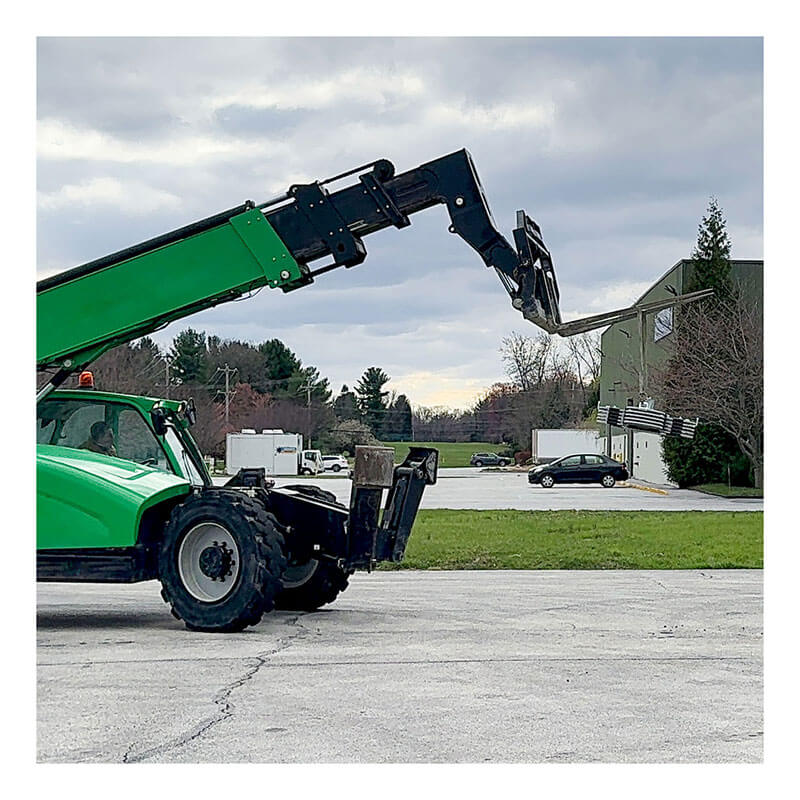 A green telescopic forklift is parked near cars and a large building, suggesting the use of Frontline Fall Protection's Frontline Commando Counterweight Fall Protection System CO2NN under the cloudy sky.