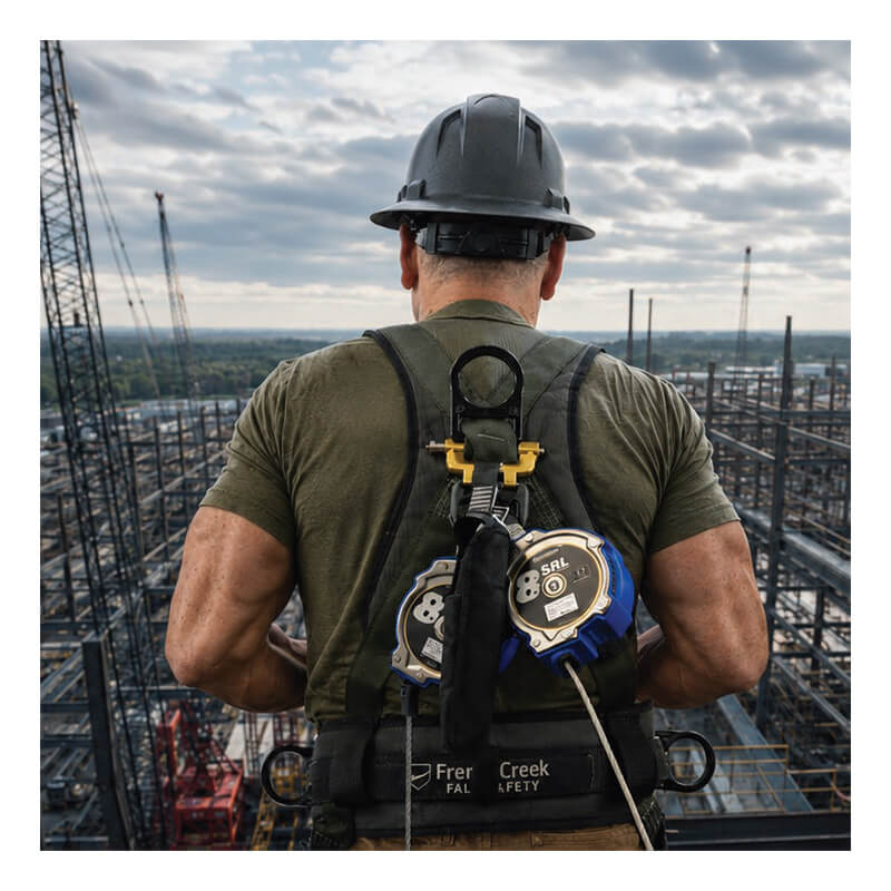 A construction worker in a hard hat uses the French Creek 8’ Class 2 Personal SRL XR_-8LE by French Creek Production while standing on a high platform, overseeing an industrial site with steel structures and cranes beneath a cloudy sky.