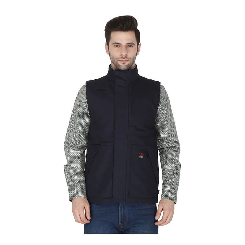 A man with short brown hair wears a ForgeFR Forge FR Canvas Duck Vest MFRVST-001 (NFPA2112-compliant, black) over a light gray patterned shirt and blue jeans, standing and facing forward against a plain white background.