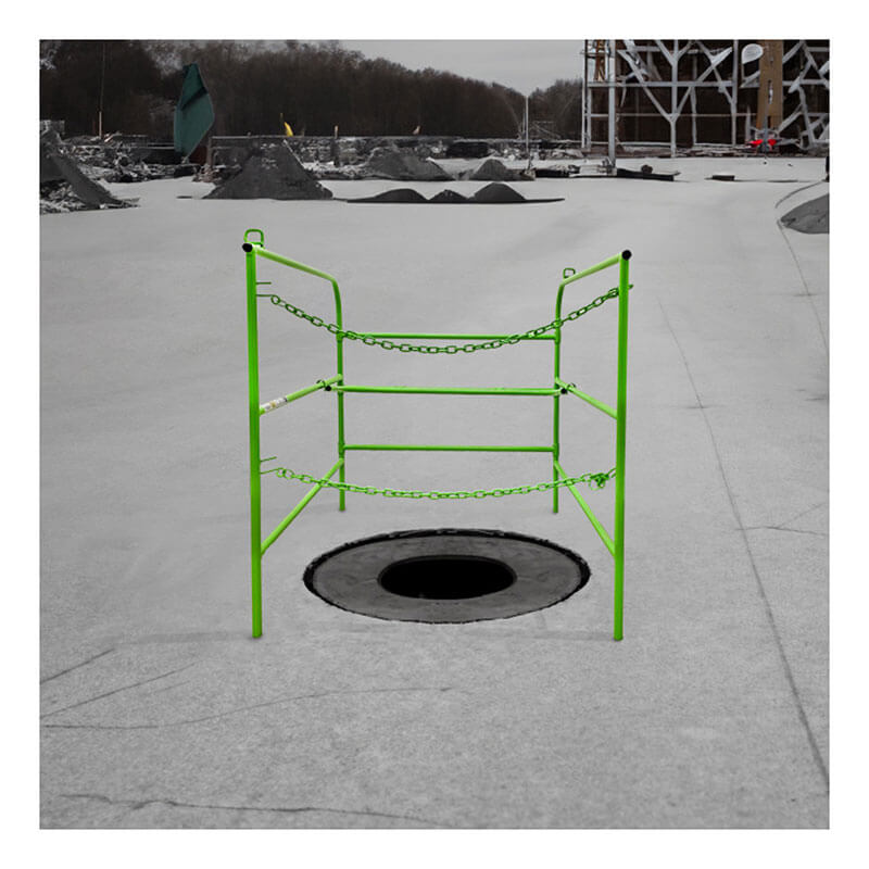 A construction site displays a circular hole secured by the Frontline Manhole Guardrail from Frontline Fall Protection, its bright green guardrail and chains ensuring confined space safety. Equipment and unfinished structures sit nearby under a cloudy sky.