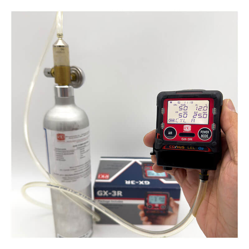 A hand calibrates a gas detector with the RKI Instruments Gas Monitor Calibration Service, showing the device connected to a silver calibration cylinder. An RKI Instruments GX-3R box and monitors appear in the background on a white surface.