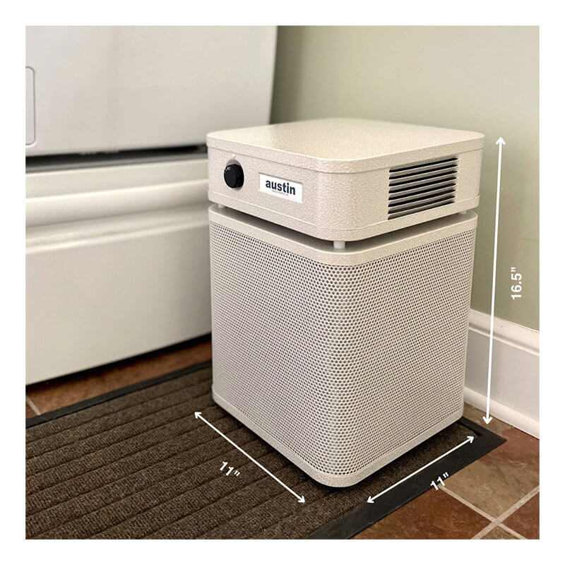 A beige Austin Air Systems HealthMate Plus Junior Machine A250 air purifier with a Medical Grade HEPA filter sits on a brown floor mat beside a wall and white appliance, measuring 11 inches wide and 16.5 inches tall.