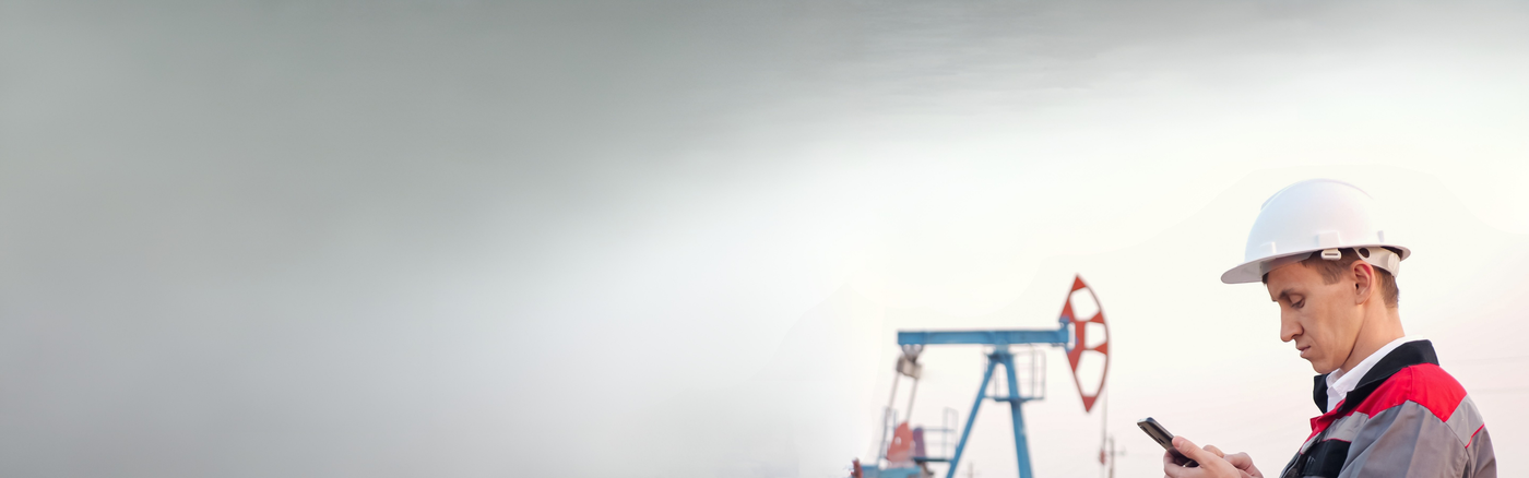 Person in a hard hat using a phone next to an oil pumpjack on a plain background