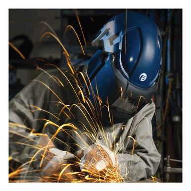 A worker wearing protective gear, including a PureFlo 3000 PAPR Welding respirator and a blue helmet, operates a grinder, sending bright sparks flying. The dimly lit workshop background enhances the contrast with the vivid spark trails.