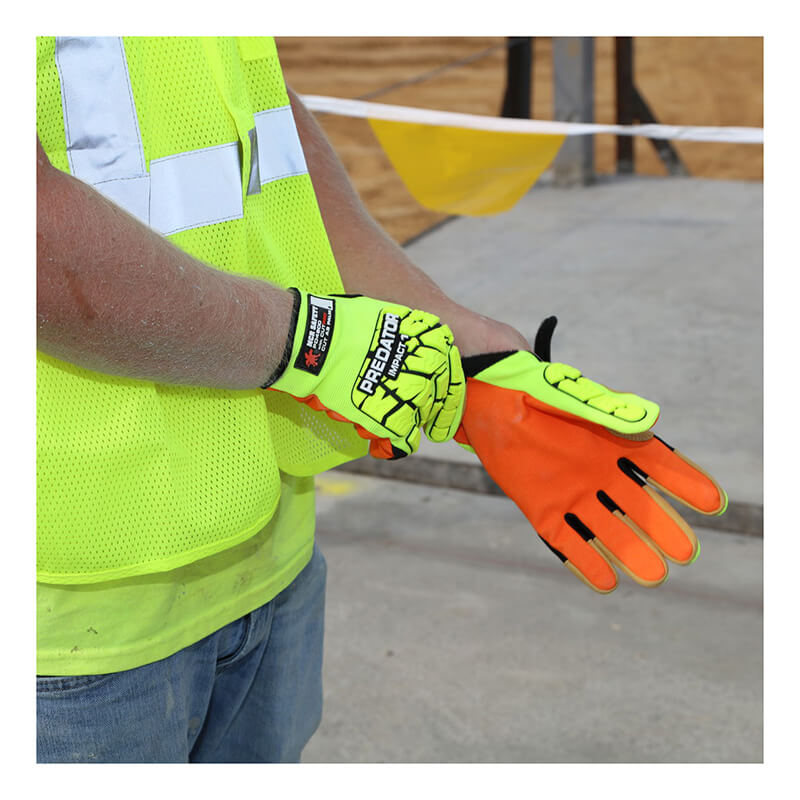 A person wearing a hi-vis vest is adjusting a pair of MCR Safety Predator Impact 1 MAXGrid Hi-Vis CutPro Gloves PD4900, which are bright orange and yellow with black protective accents, on a construction site. These gloves ensure impact resistance and offer superior Kevlar cut protection. In the background, caution tapes and construction materials are visible.