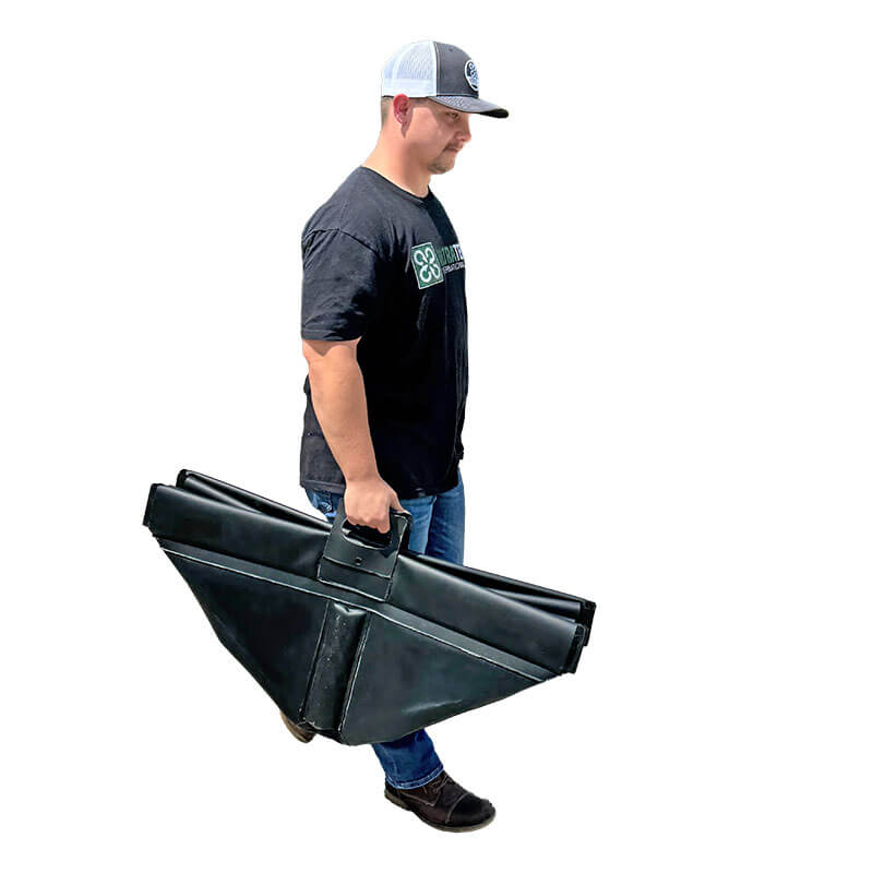 A man in a baseball cap, black T-shirt, jeans, and boots carries the UltraTech Pellet Pond 8859 by UltraTech—a large, folded black metal pellet retention system with handle—walking against a white background.