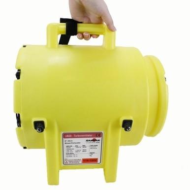 A person holds a Euramco RamFan UB20 Blower and Duct/Canister, a compact and portable device colored yellow with an ergonomic handle. This blower, intended for ventilation or air circulation, is equipped with a power switch and features a labeled panel on the side. Its UV-resistant casing ensures durability across diverse environments.