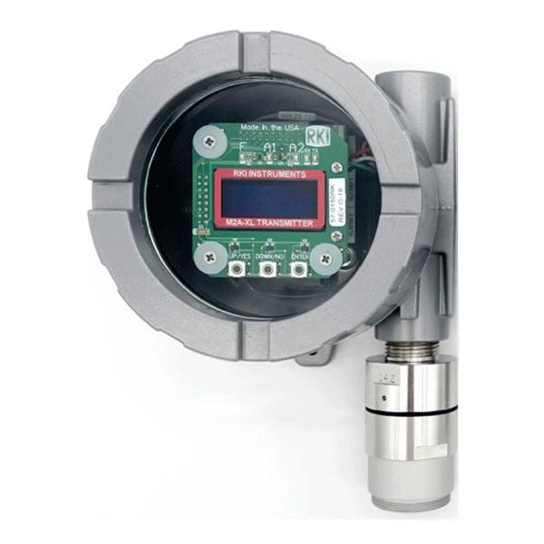 A gray RKI Explosion Proof M2A-XL Transmitter with an exposed circuit board and a digital display showing "RKI Instruments" and "M2A-XLF TRANSMITTER," featuring a cylindrical LEL sensor on the right.