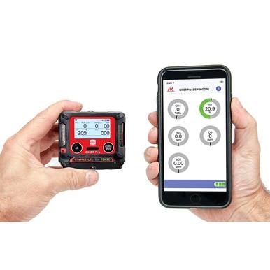 In two hands are devices: one holding the RKI GX-3R Pro 5 Gas Confined Space Monitor from PK Safety Supply, showing "209," and the other grasping a smartphone with wireless communication, displaying a connected app that features digital gauges and readings such as "20.9.