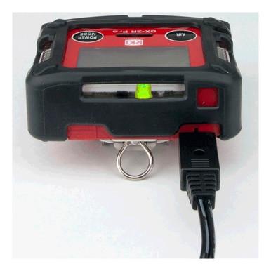 A close-up of the RKI GX-3R Pro 5 Gas Confined Space Monitor by PK Safety Supply showcases its sleek black and red design, featuring a digital display and buttons. The monitor is equipped with a cable connection at the bottom, and its screen displays a bright green indicator light, ensuring effective personal monitoring for safety in complex environments through wireless communication.