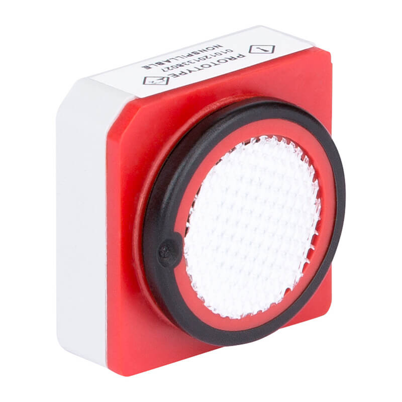 A close-up of a square, red and white photo reflector with a round, textured reflective surface bordered by a black ring. This compact device is often paired with industrial sensors like the BW Technologies by Honeywell SR-M1-1S CO Sensor.