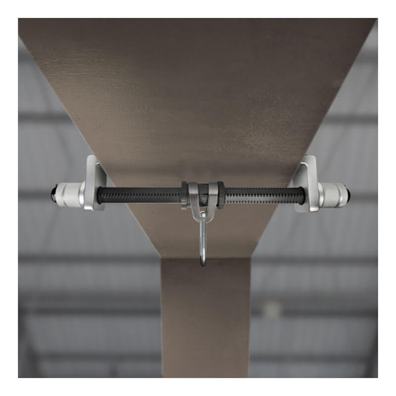 A close-up of the Frontline Aluminum Sliding I-Beam Anchor by Frontline Fall Protection secured to an I-beam, with a blurred industrial ceiling in the background.