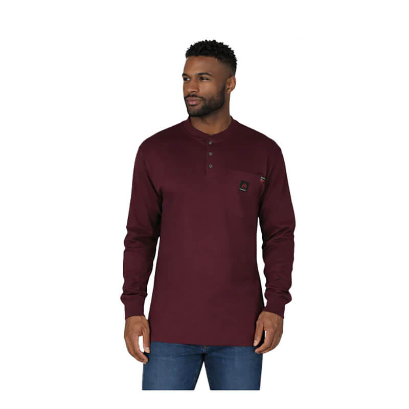 A man wears the ForgeFR Forge FR Henley MFRHNLY-004, a long-sleeve burgundy FR shirt with a chest pocket, and blue jeans against a plain white background.