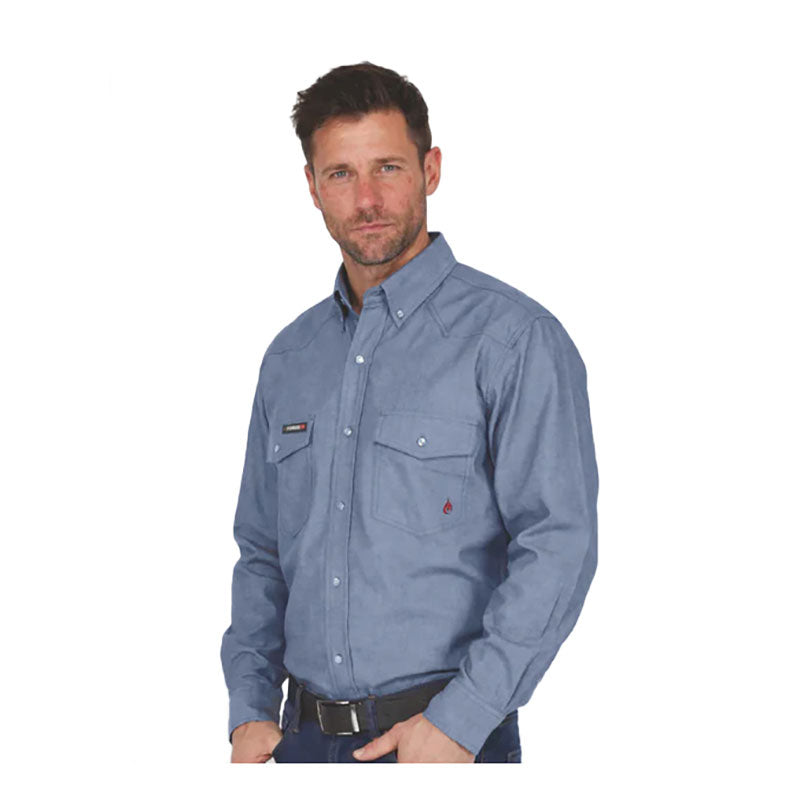 A man with short brown hair and a beard is wearing the ForgeFR Forge FR Chambray Shirt MFRCLS0010, featuring chest pockets, along with dark pants, and is standing against a white background.