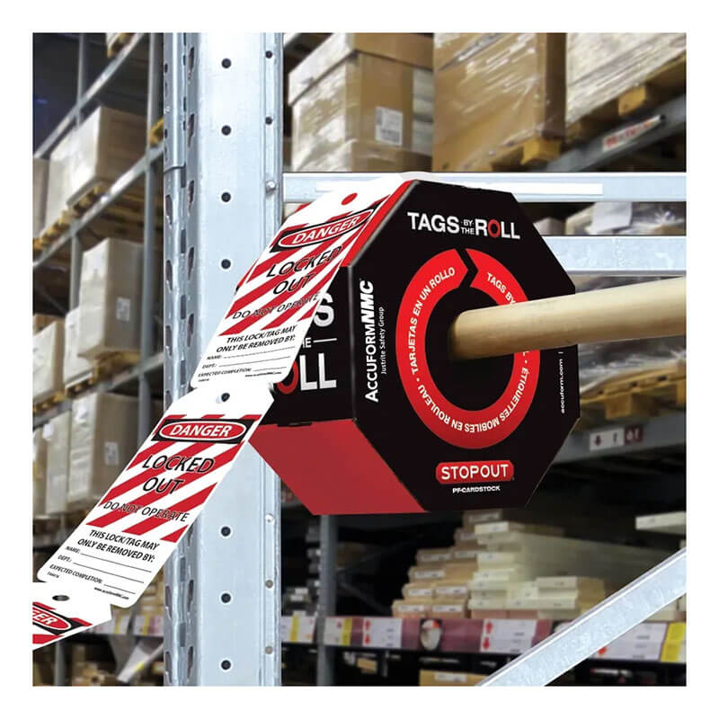 A roll of Accuform OSHA Danger Tags By-The-Roll: Locked Out Do Not Operate (OSHA Style) from AccuformNMC is displayed on a dispenser on a metal shelving unit in the warehouse. Featuring OSHA-compliant red and white warning stripes with bold black text, these tags stand out clearly against the boxes visible on shelves in the background.